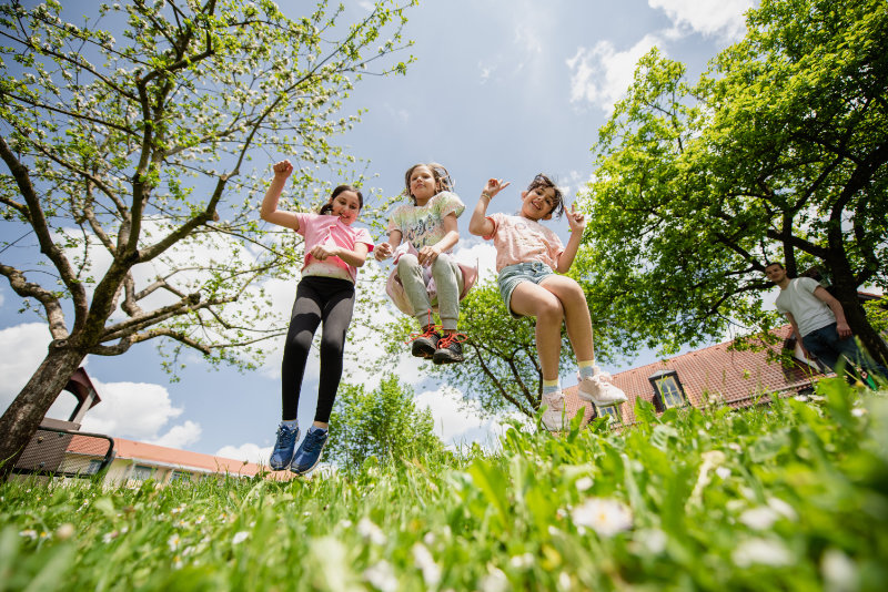 drei Kinder hüpfen im grünen Gras Richtung Himmel